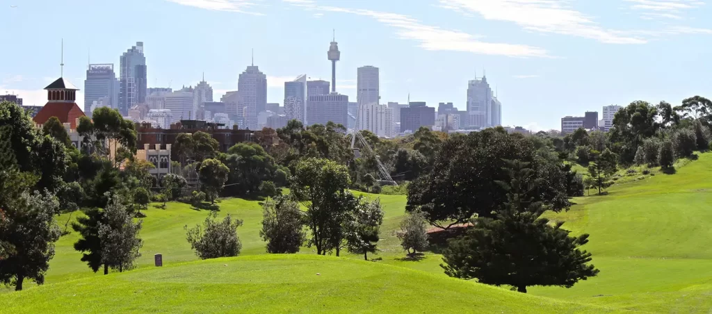 Moore Park Golf Course with green fairways and trees in the foreground, and Sydney’s city skyline with the Sydney Tower in the background.