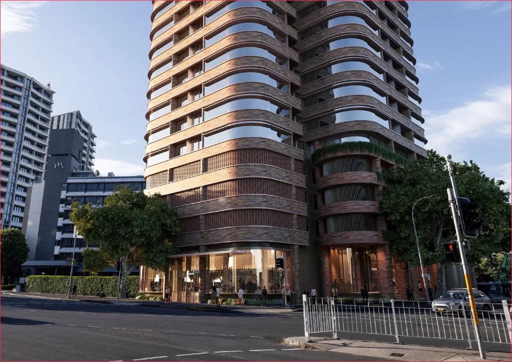 A modern dual-tower development featuring a curved, Art Deco-inspired brick façade, with large glass windows and greenery integrated into the design. The street-level includes retail spaces and a vibrant urban streetscape with trees and pedestrians, located in Newcastle West.