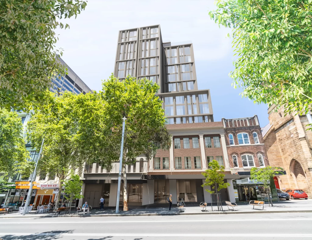 A digital render of a proposed 14-storey mixed-use development at 806-812 George Street, Haymarket, Sydney. The image showcases a modern high-rise building integrated with a retained heritage façade, featuring large windows and a stepped architectural design. Green trees line the street, and adjacent heritage buildings, including Christ Church St Laurence, are visible. Pedestrians and outdoor dining areas are present at street level.