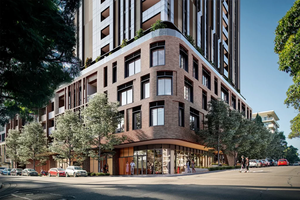 A modern mixed-use high-rise development with a brick-clad podium, large windows, and greenery on terrace levels. The ground floor features retail spaces with people walking by, while trees line the street. Cars are parked along the curb, and a bright blue sky is visible in the background.