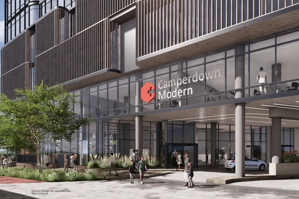 Architectural rendering of the entrance to the Camperdown Modern Private Hospital, featuring a glass facade with the hospital’s logo displayed above. Several pedestrians are walking near the landscaped plaza, while a car is seen entering the drop-off area.