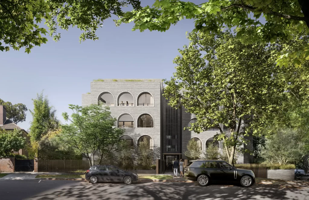 A modern, five-story residential building with arched windows and a grey brick facade, surrounded by lush greenery and parked cars along the street.