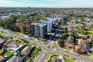 Aerial view of a suburban neighborhood in NSW, Australia, showing a mix of low-density detached houses and modern mid-rise apartment buildings, with tree-lined streets, roundabouts, and cars on the roads.