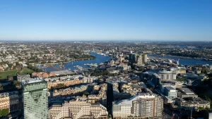 Aerial view of Sydney’s Pyrmont and Darling Harbour area, showcasing high-rise buildings, waterfront developments, and the Anzac Bridge under a clear blue sky.