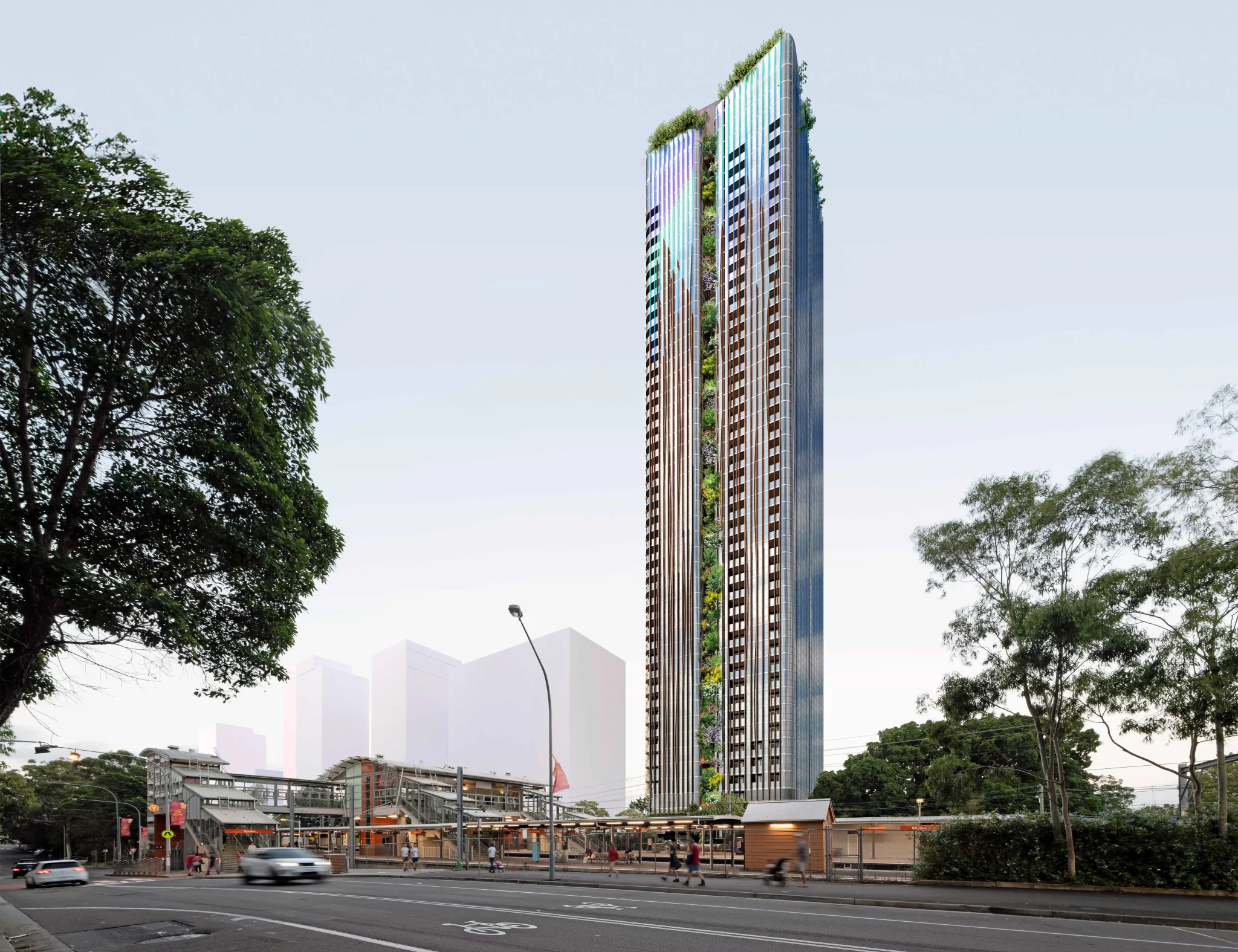 A 48-storey mixed-use tower with a vertical green façade rises above Rhodes train station in Sydney’s Eastern Harbour City. The skyscraper features sleek glass and metallic cladding, with greenery integrated into the central vertical strip and rooftop. Trees and pedestrians line the foreground, while the station and urban infrastructure sit below.