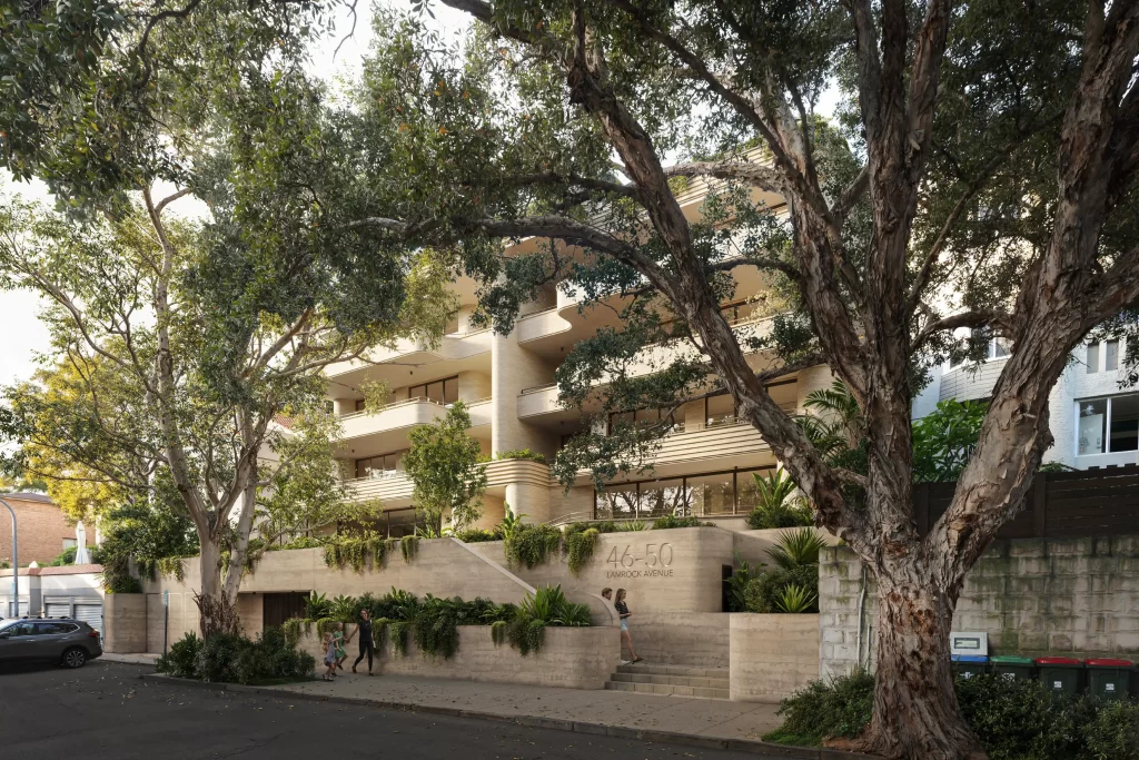 A modern five-storey residential building at 46-50 Lamrock Avenue, Bondi Beach, featuring curved balconies, lush landscaping, and a concrete façade. Large trees frame the view, and pedestrians walk along the footpath.