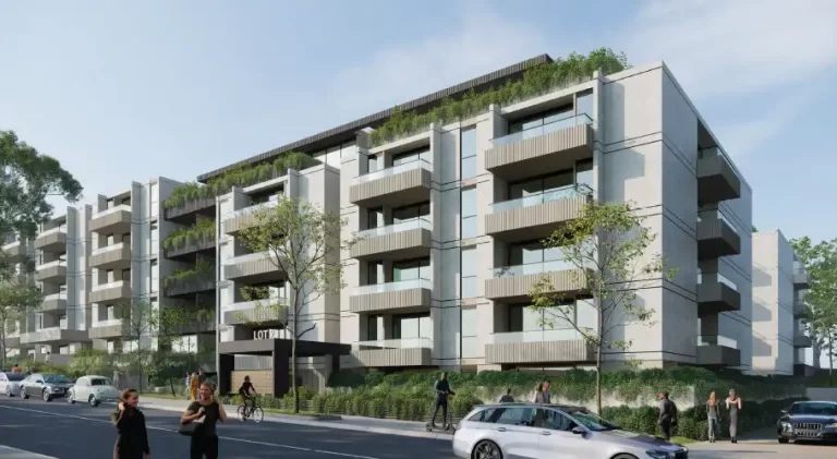 A modern, mid-rise residential apartment complex featuring multiple five-story buildings with glass balconies, green rooftop gardens, and a landscaped streetscape. Pedestrians, cyclists, and vehicles are visible along the tree-lined road in front of the development.