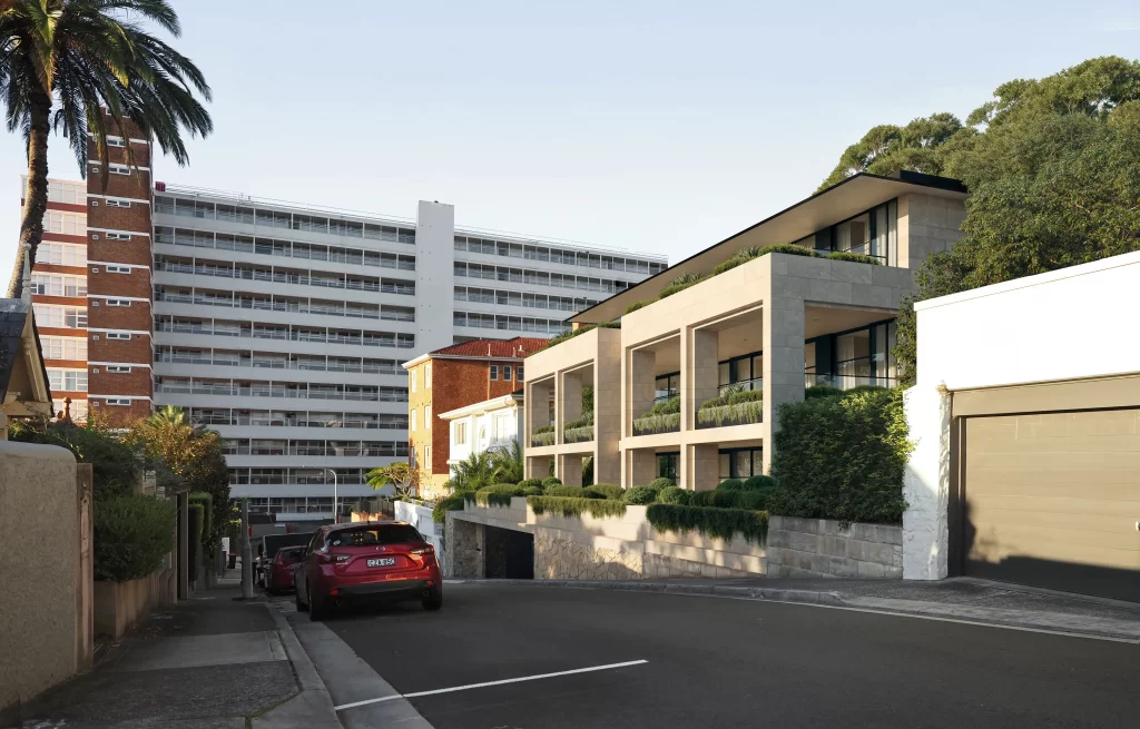 A photomontage of a proposed boutique apartment development at 7 Annandale Street, Darling Point. The modern, low-rise building features a sandstone-like façade, large balconies with greenery, and a landscaped setback. The development contrasts with the taller brick and white high-rise apartment building in the background. A tree-lined residential street with parked cars leads up to the property.