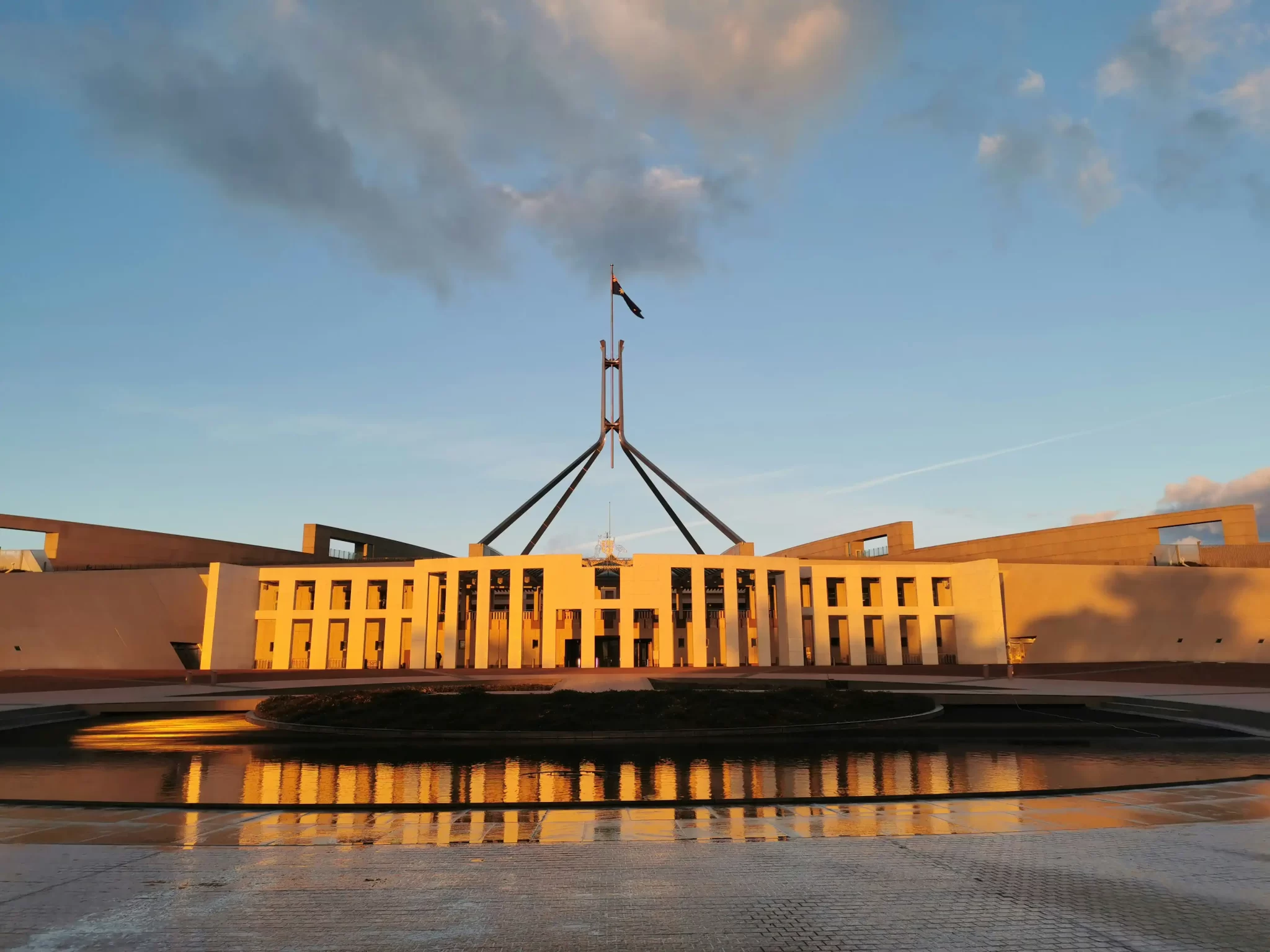 Parliament House in Canberra at sunrise, reflecting in the forecourt water feature under a clear sky.