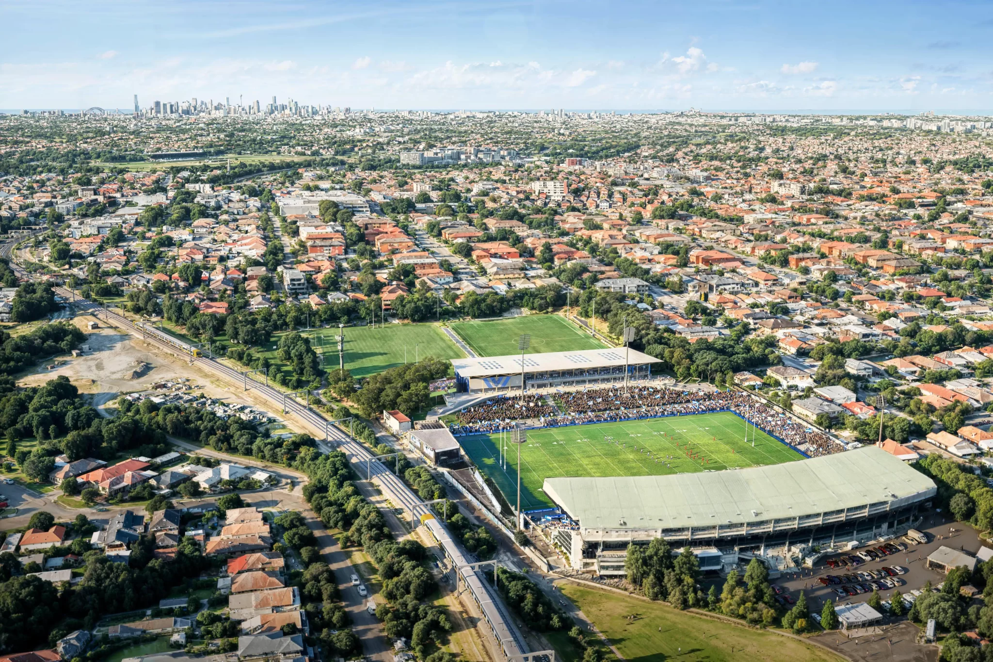 Aerial view of Belmore Sports Ground and surrounding suburb with Sydney CBD skyline in the distance.