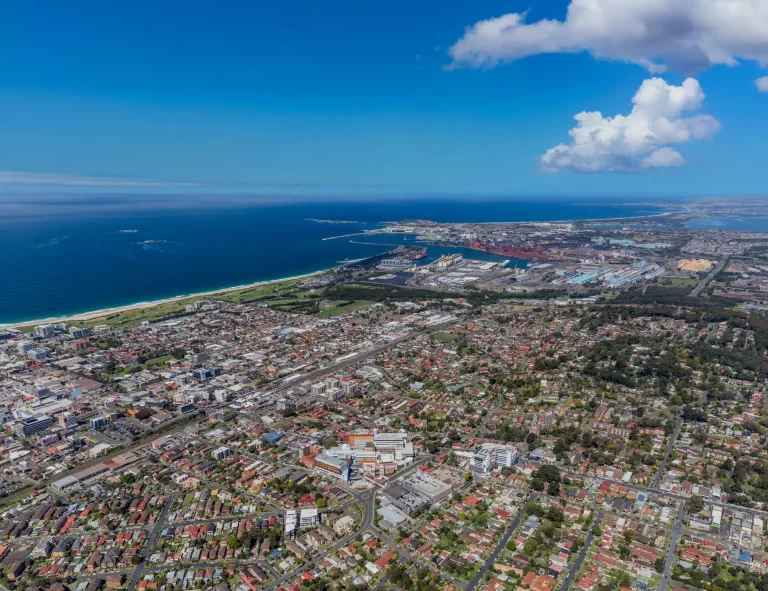 Aerial view of Wollongong city and coastline, featuring urban development, Wollongong Harbour, and surrounding residential areas.