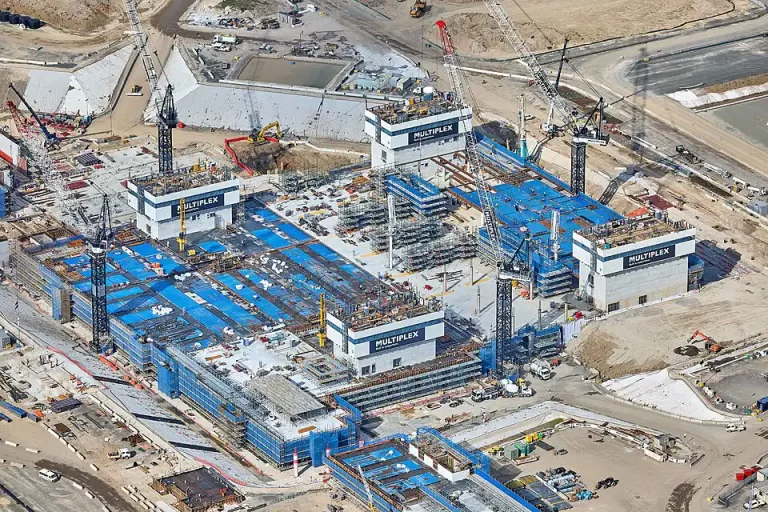 Aerial view of Western Sydney Airport under construction, showing cranes, scaffolding, and large Multiplex structures across a cleared site.